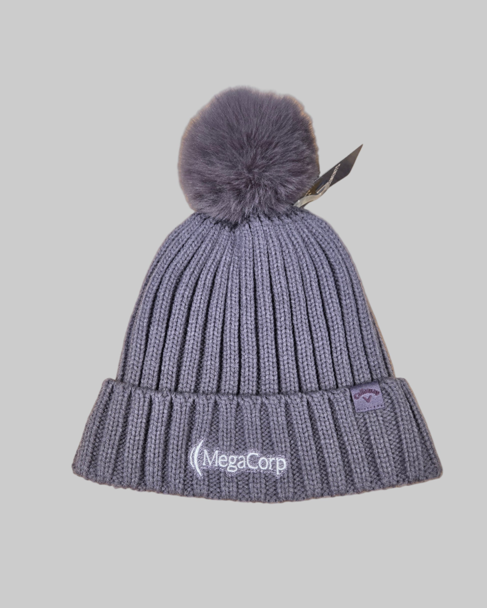 Gray knit beanie with pom-pom on a wooden surface, featuring the MegaCorp logo.